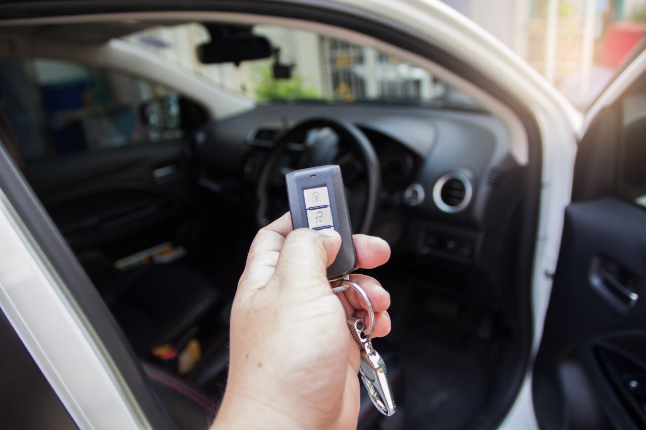 Osoba trzyma kluczyk samochodowy z jednym przyciskiem otwartym, stojąc obok otwartych drzwi pojazdu.