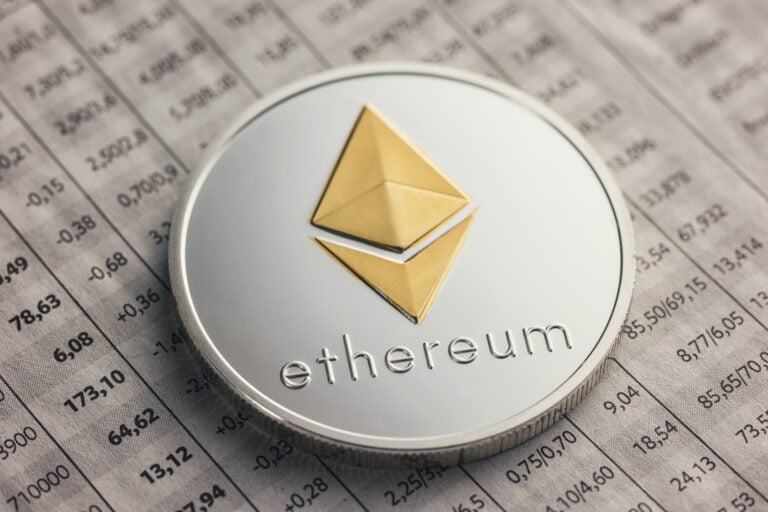 Srebrna moneta z logo Ethereum leżąca na tabeli finansowej.