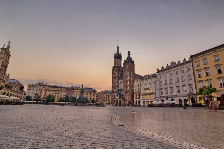 Rynek Główny w Krakowie o zmierzchu, widok na Kościół Mariacki i otaczające budynki.