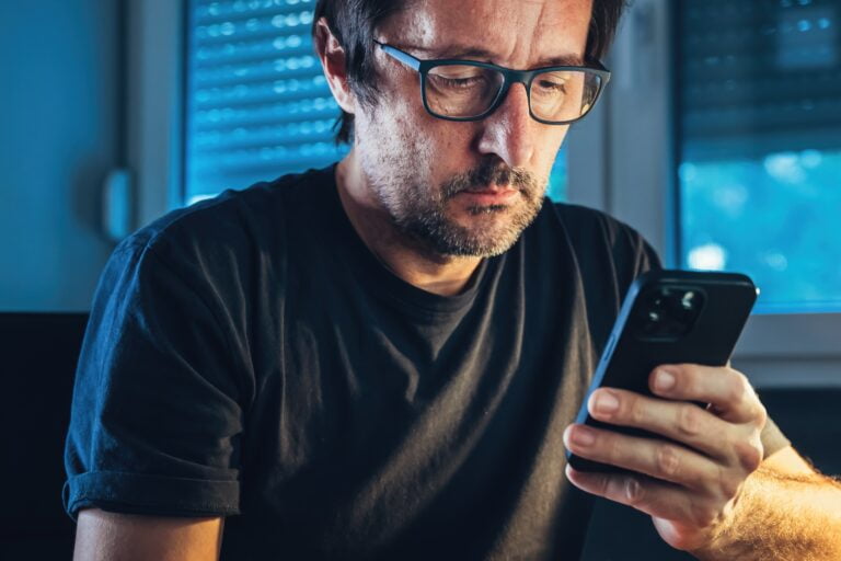 Mężczyzna w okularach i czarnej koszulce patrzy na smartfona.
