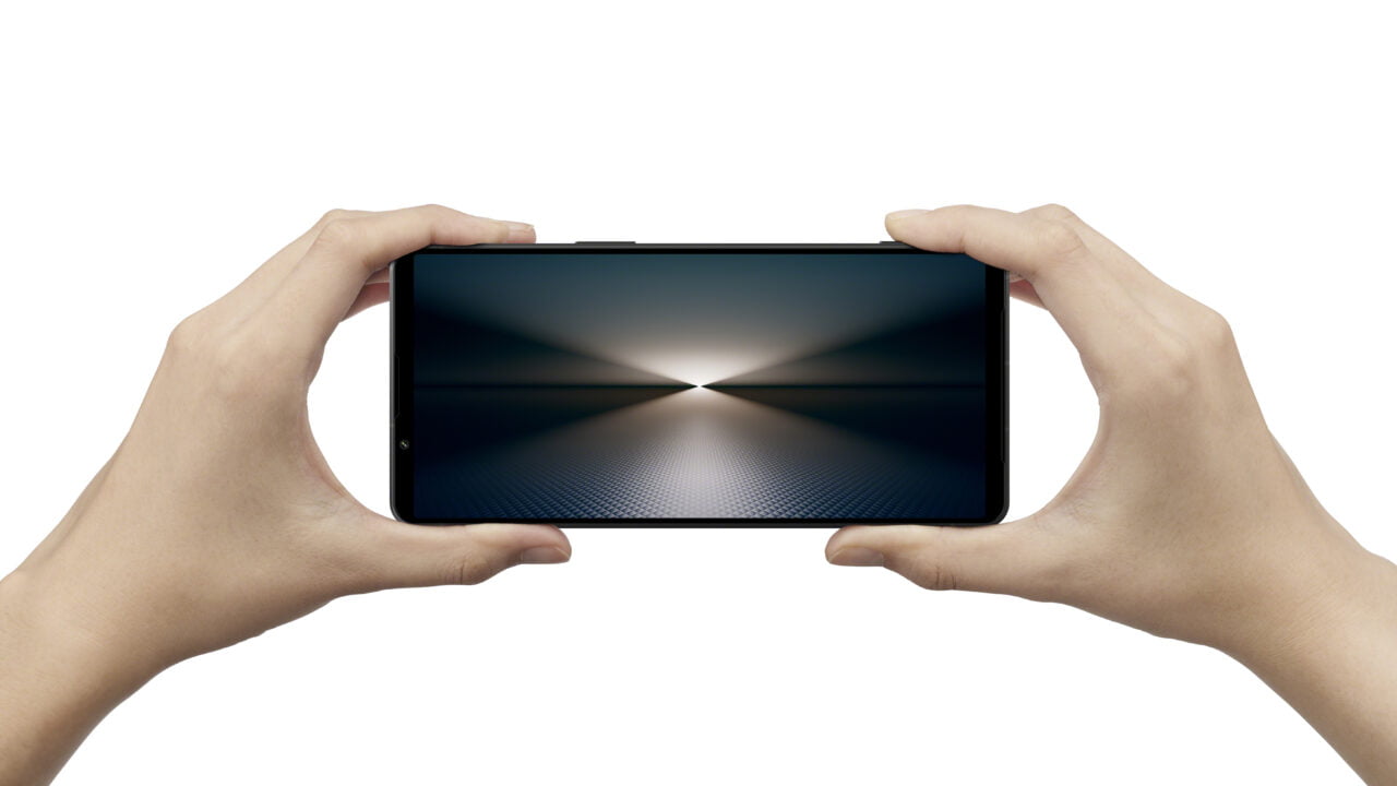 Ręce trzymające poziomo smartfon z wyświetlaczem pokazującym abstrakcyjną grafikę.