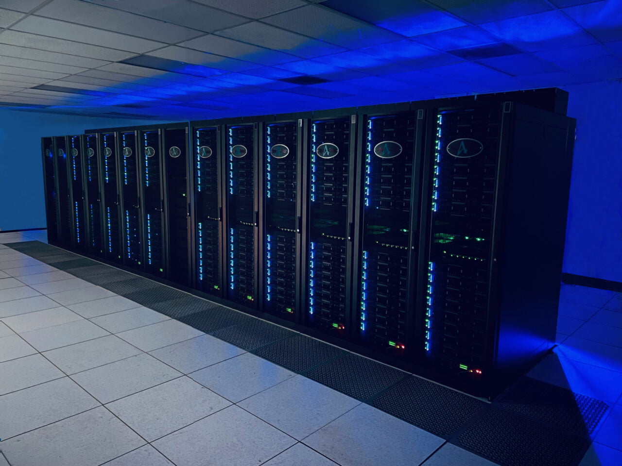 Fileira de servidores pretos em um data center com iluminação LED azul.