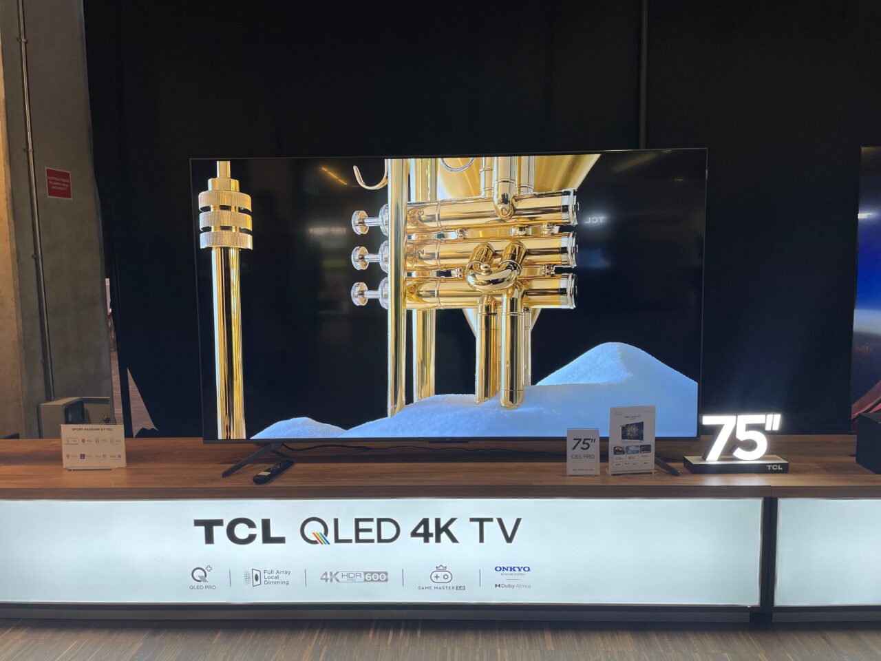 Duży telewizor TCL QLED 4K 75 cali prezentujący obraz złotej trąbki na tle śnieżnych gór.