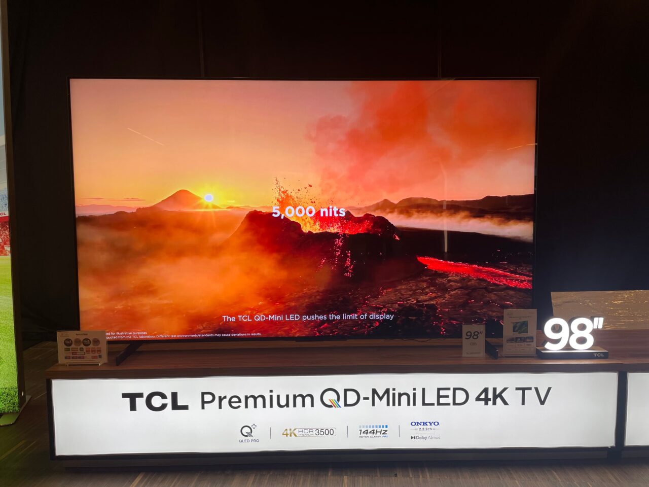 Duży telewizor TCL Premium QD-Mini LED 4K o przekątnej 98 cali wyświetlający obraz aktywnej wulkanicznej lawy i zachodzącego słońca.