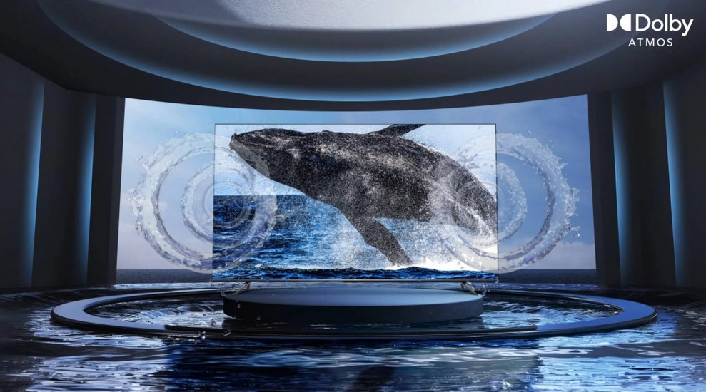 Wieloryb wynurzający się z morza na ekranie wewnątrz futurystycznego pomieszczenia z logo Dolby Atmos w prawym górnym rogu.