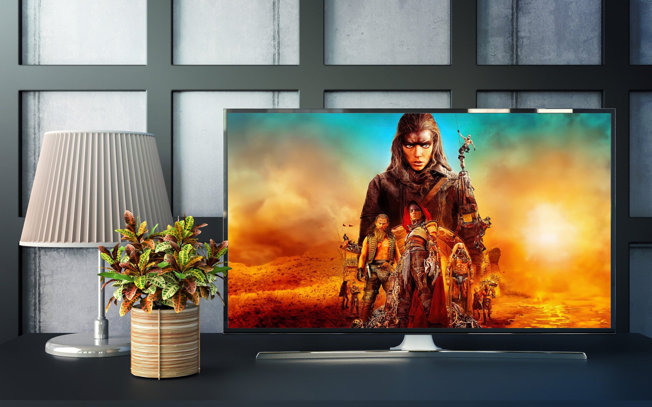 Telewizor na stole, obok lampka i doniczka z rośliną; na ekranie scena z filmu akcji w postapokaliptycznym świecie.