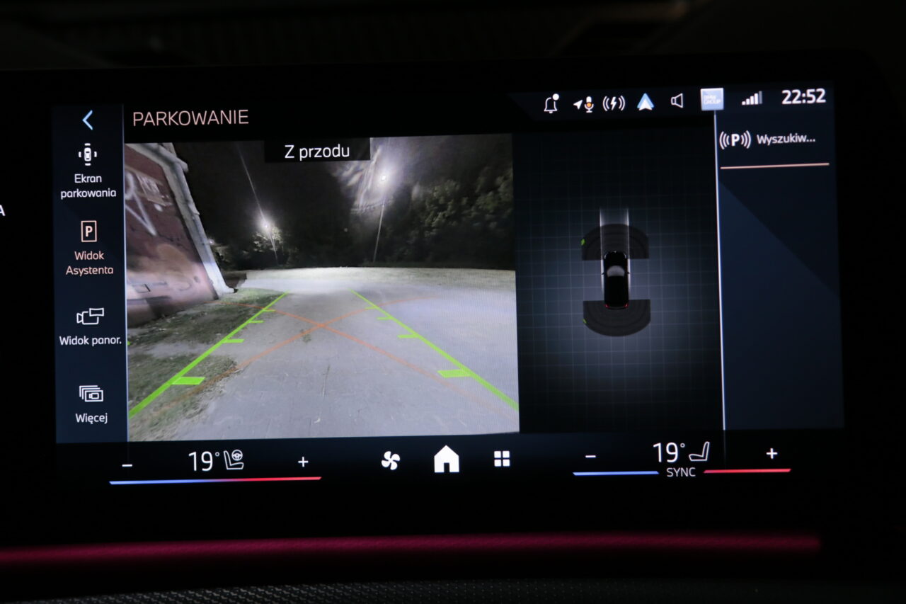 Widok z kamery cofania samochodu wyświetlający podświetlony park uliczny w nocy, z graficzną reprezentacją samochodu widoczną po prawej stronie ekranu.