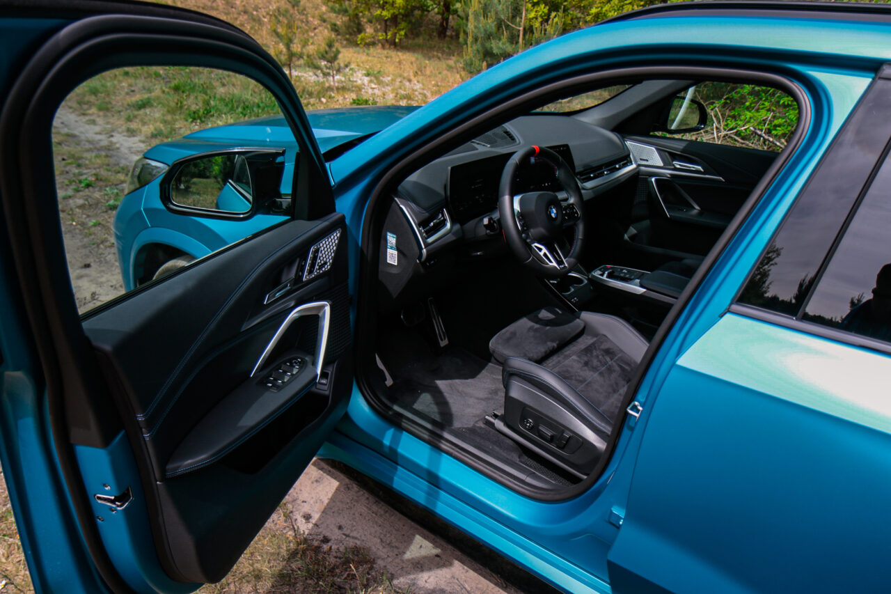Wnętrze BMW X1 M35i podczas testu, widok z otwartymi drzwiami na kierownicę i deski rozdzielczej.