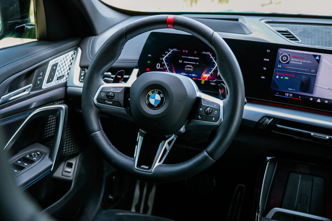 Wnętrze BMW X1 M35i podczas testu, pokazujące kierownicę i deski rozdzielczej z wyświetlaczami.