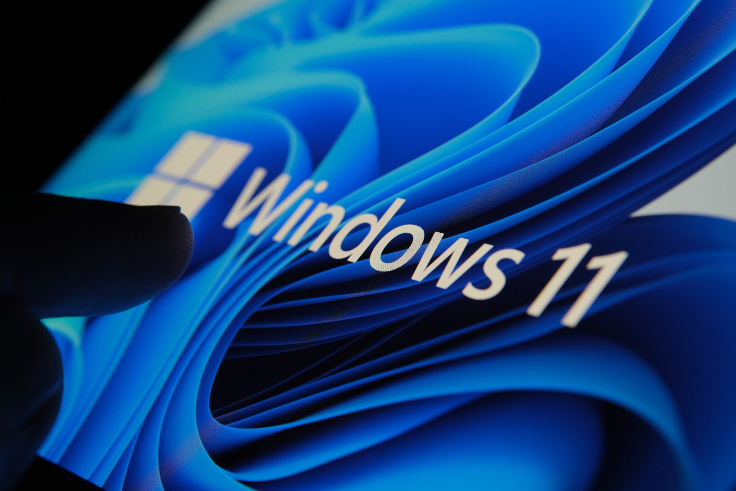 Zbliżenie na ekran z logo Windows 11 i abstrakcyjnym niebieskim tłem.