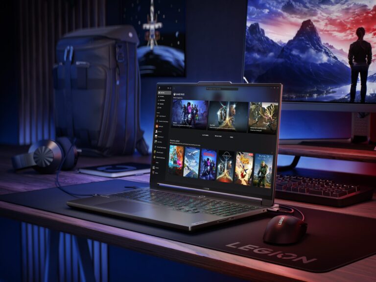 Laptop Legion na biurku w przyciemnionym pokoju, z plecakiem, słuchawkami i monitorem w tle. Na ekranie laptopa widać listę gier.