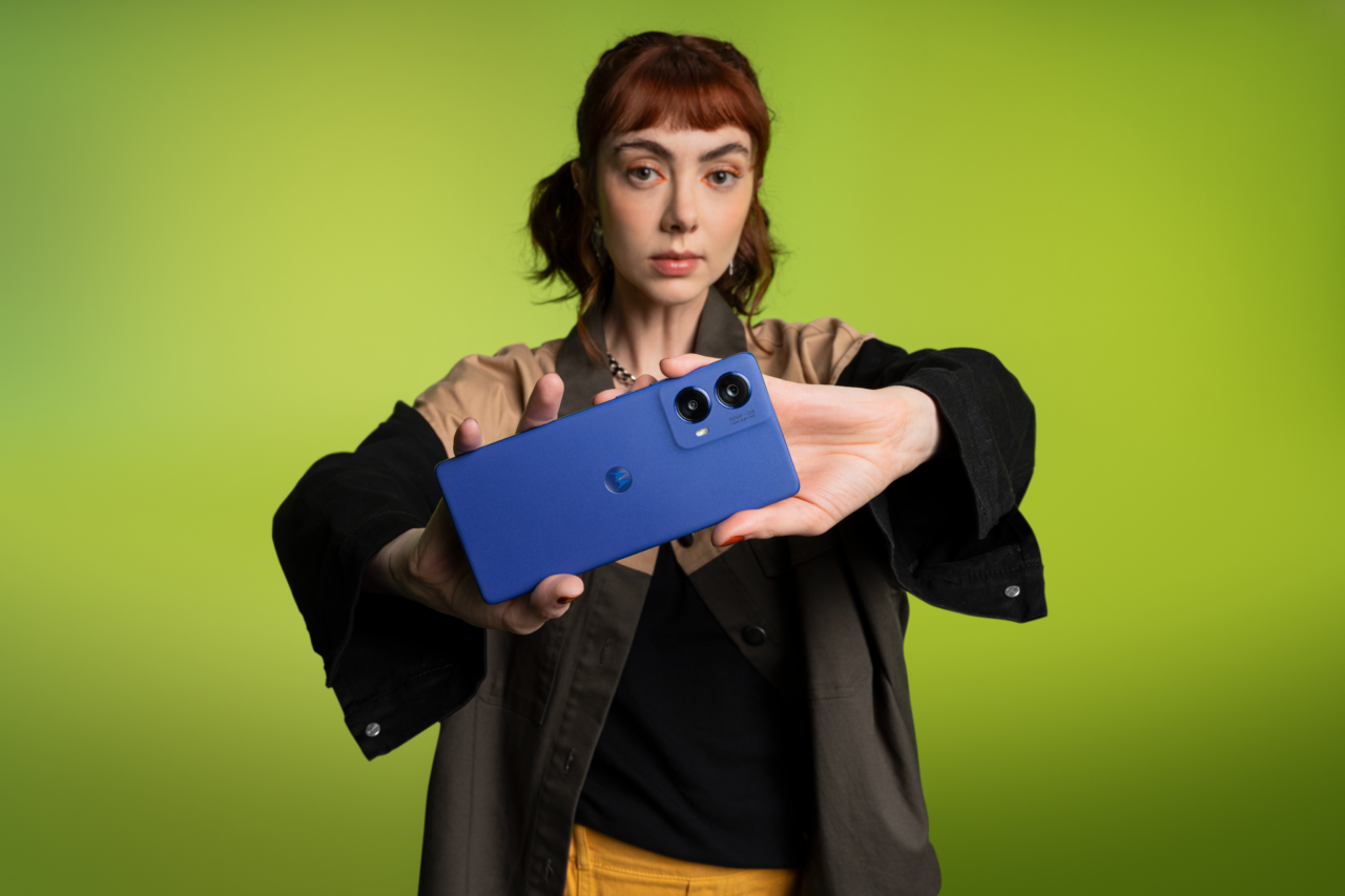 Motorola moto g85 5G. Kobieta trzymająca niebieski smartfon, na zielonym tle.