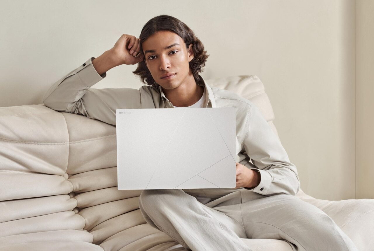 Mężczyzna siedzi na kremowej kanapie i trzyma laptopa ASUS Zenbook.