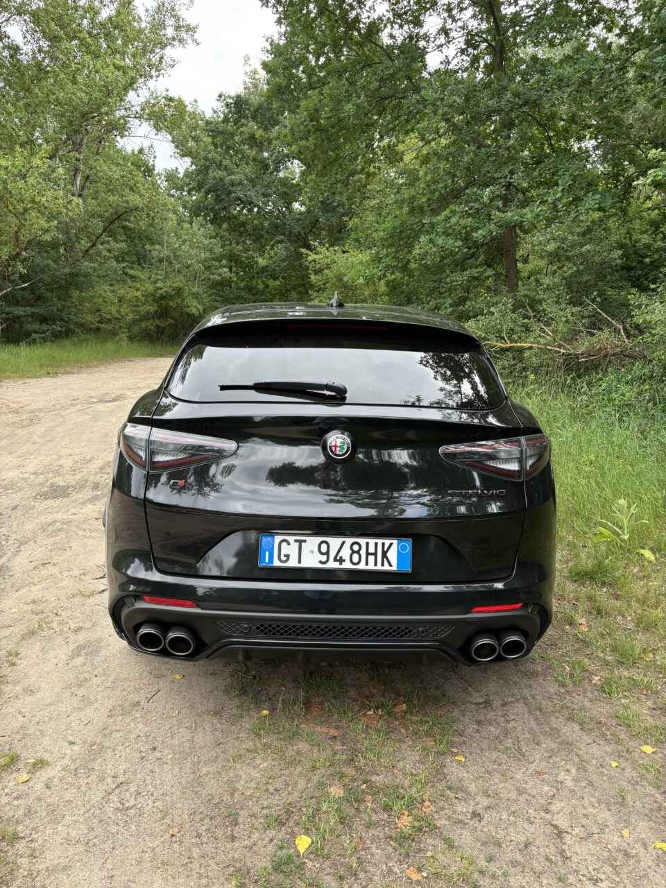 Czarny samochód marki Alfa Romeo Giulia Quadrifoglio, zaparkowany na leśnej drodze, widok od tyłu.