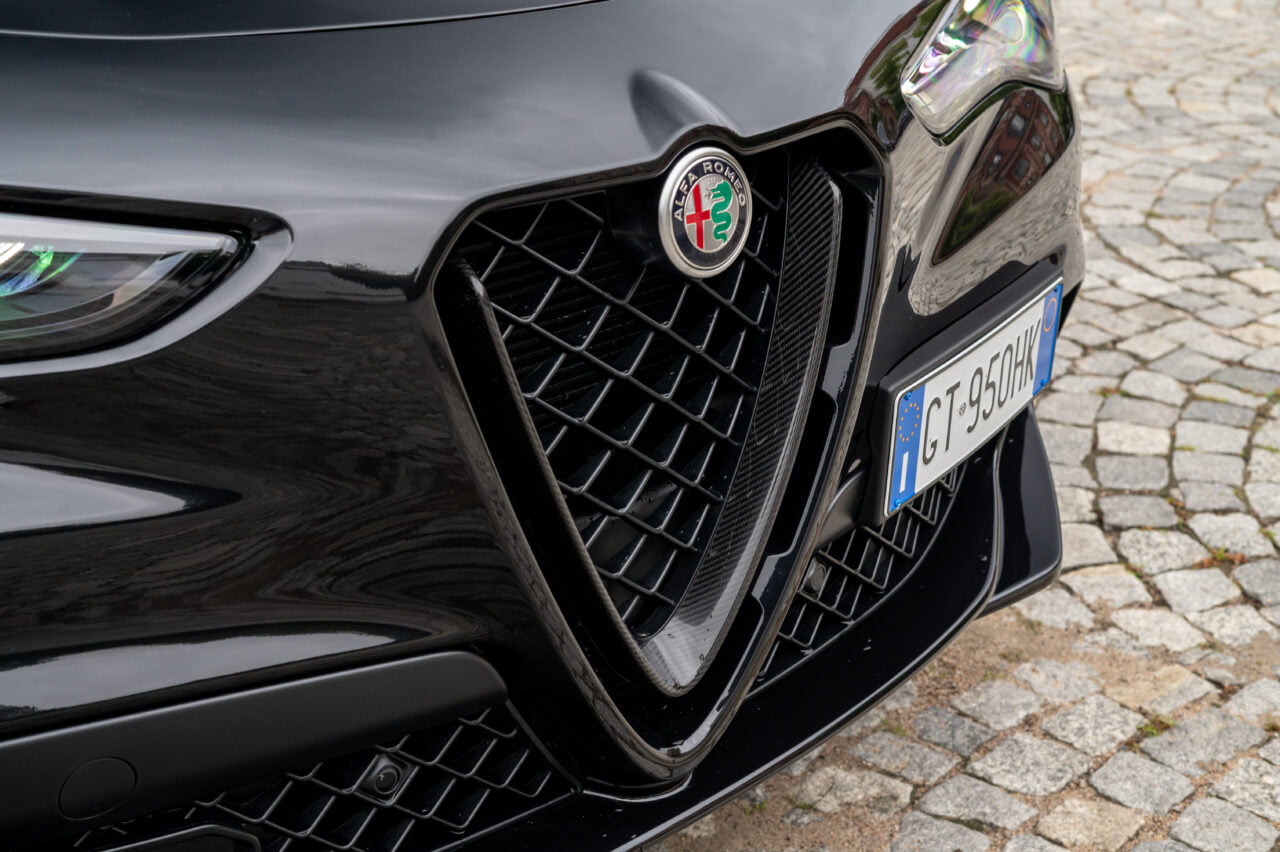Zbliżenie na przednią kratkę samochodu Alfa Romeo z widoczną tablicą rejestracyjną GT 950 HK na brukowanej nawierzchni.