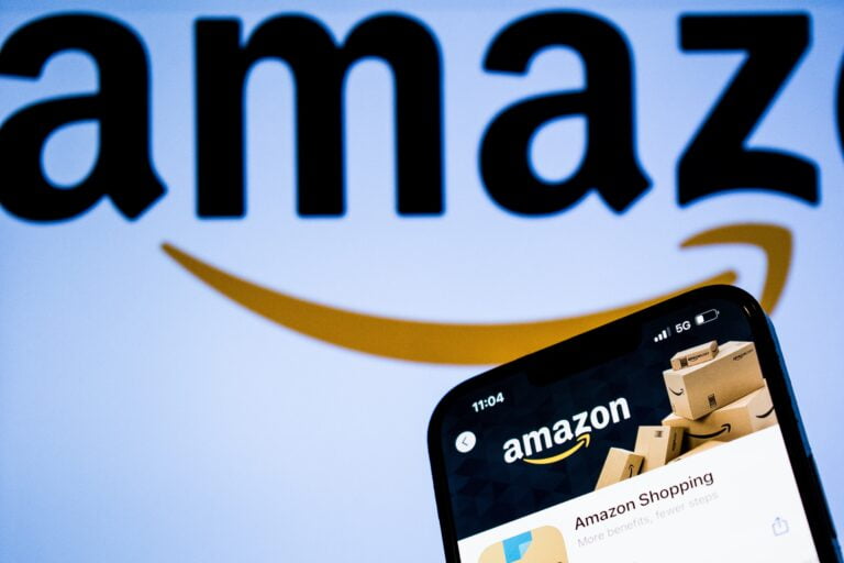 Logo Amazon na ekranie w tle oraz aplikacja Amazon Shopping na ekranie telefonu.