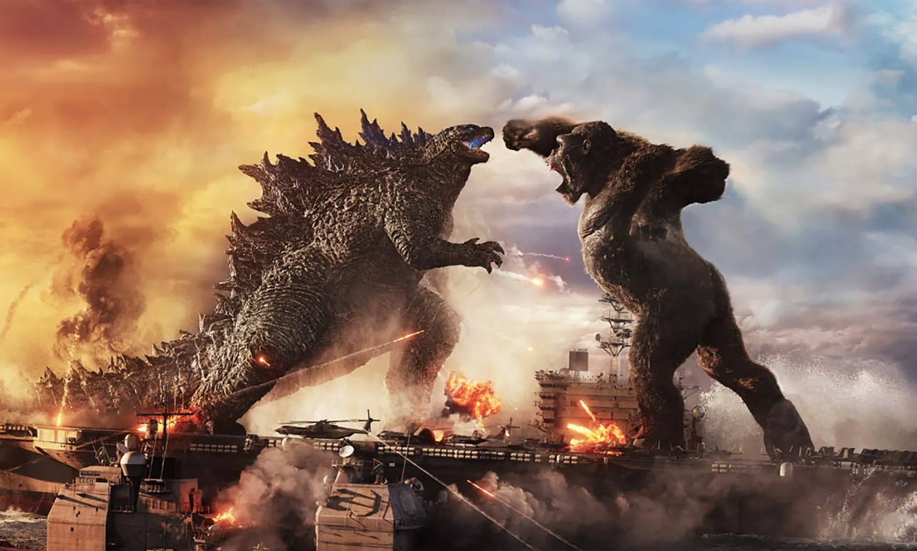 Godzilla walcząca z King Kongiem na statku wojskowym na morzu, wokół eksplozje i dym.
