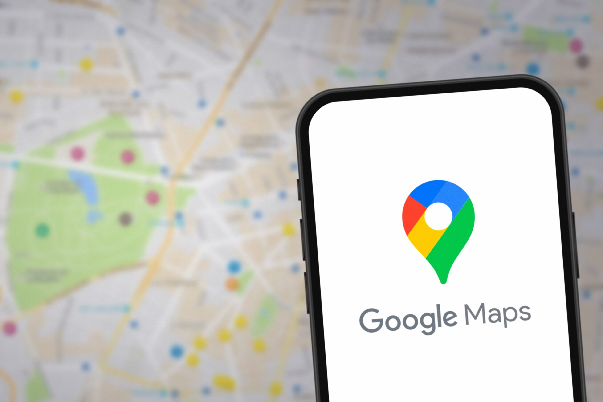Ekran smartfona z logo Google Maps na tle rozmytej mapy.