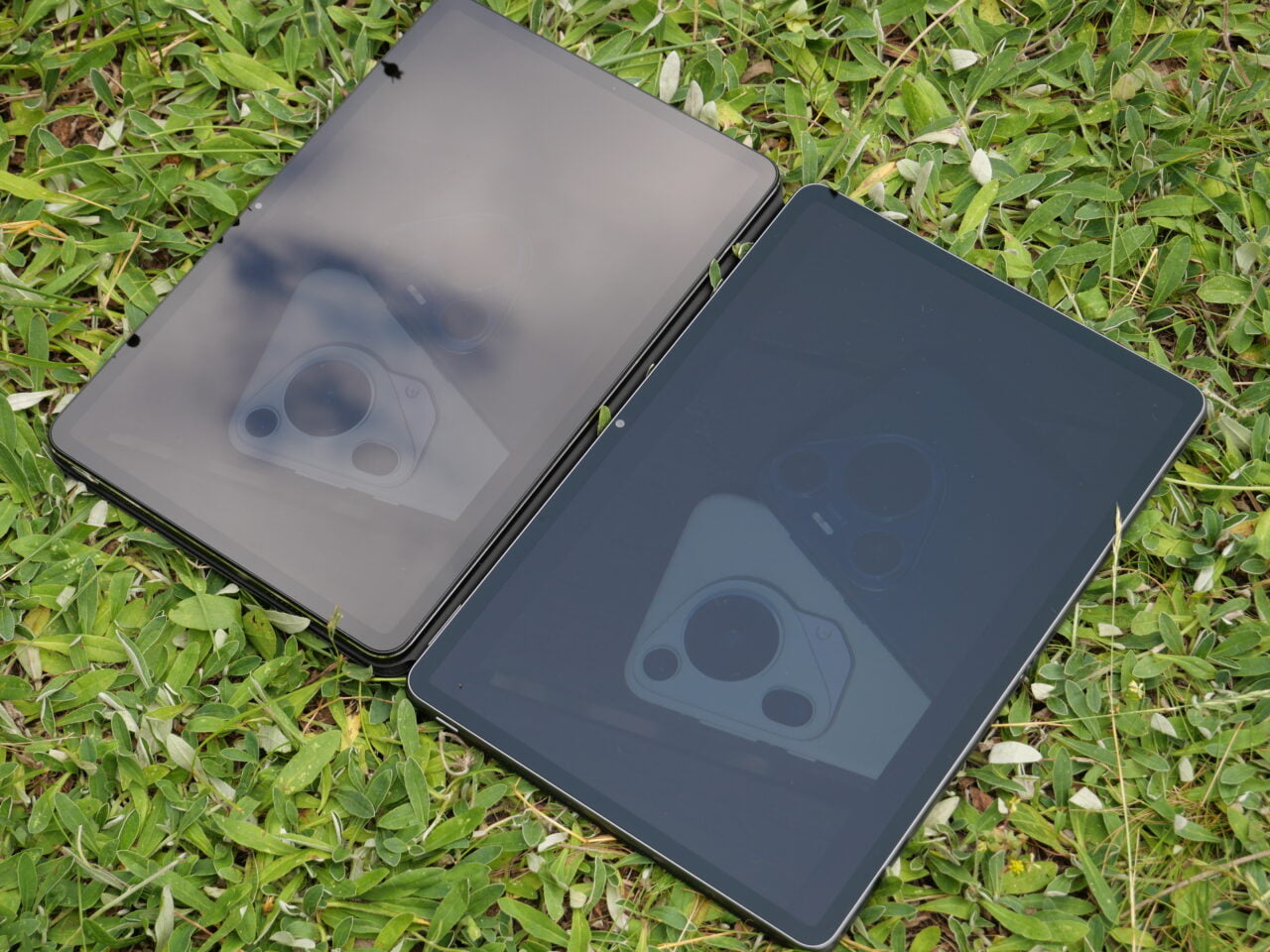 Dwa tablety leżące na trawie, z odbiciem kamery na ekranach.