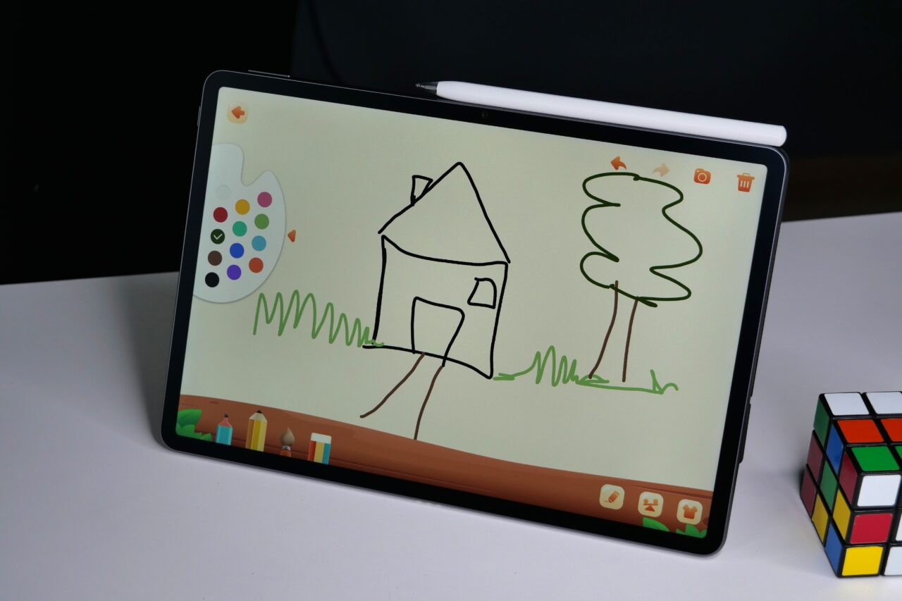 Tablet z rysunkiem domu i drzewa oraz kostką Rubika na biurku.
