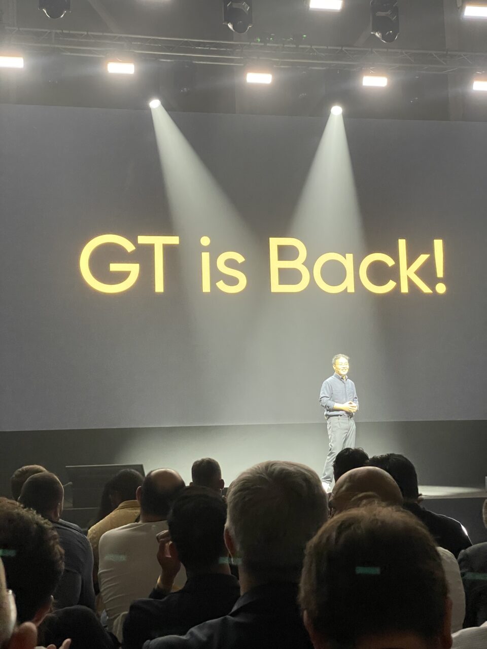 Premiera realme GT 6 Mężczyzna stoi na scenie przed publicznością, za nim na ekranie napis "GT is Back!".