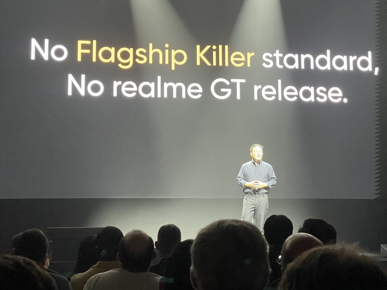 Mężczyzna na scenie prezentuje przed dużym ekranem z napisami "No Flagship Killer standard, No realme GT release."