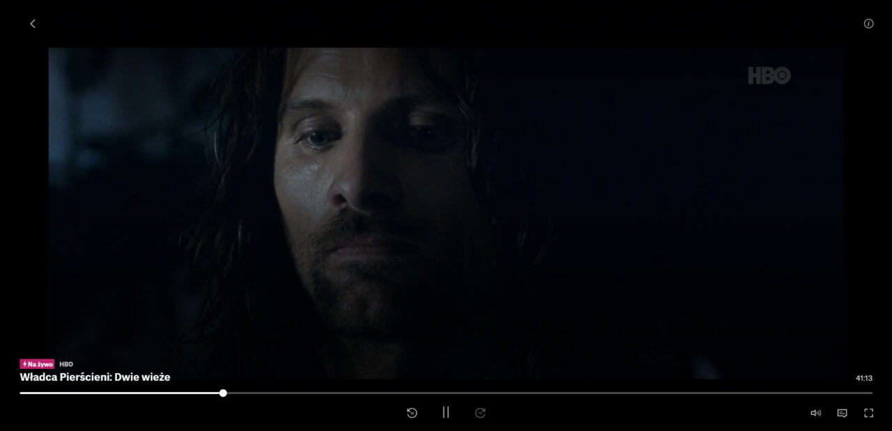 Zbliżenie twarzy mężczyzny z brodą na ciemnym tle, napis "Władca Pierścieni: Dwie wieże" w lewym dolnym rogu ekranu.