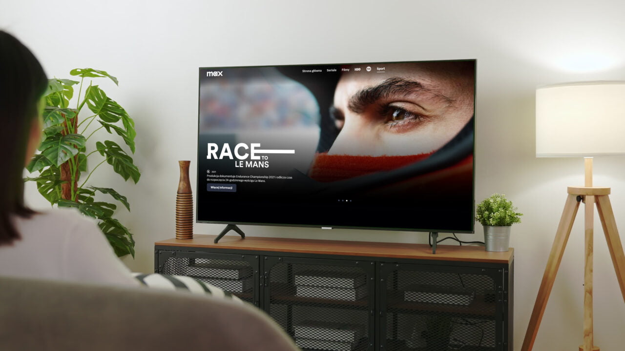 Osoba siedząca na kanapie, oglądająca na telewizorze program "Race to Le Mans" na platformie Max.