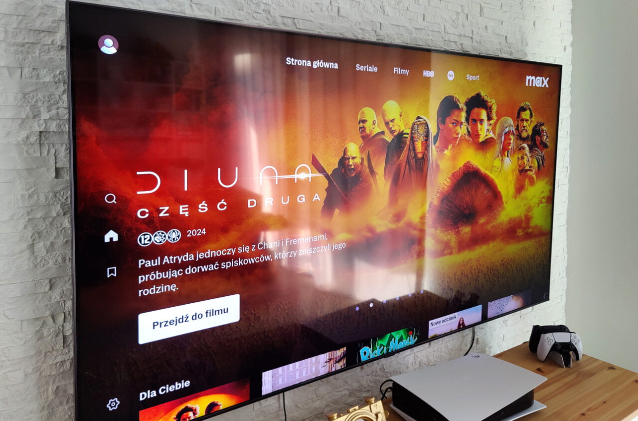 Telewizor Samsunga na ścianie wyświetlający ekran z filmu "Diuna: Część Druga" na platformie Max, obok telewizora stoi konsola PlayStation 5.