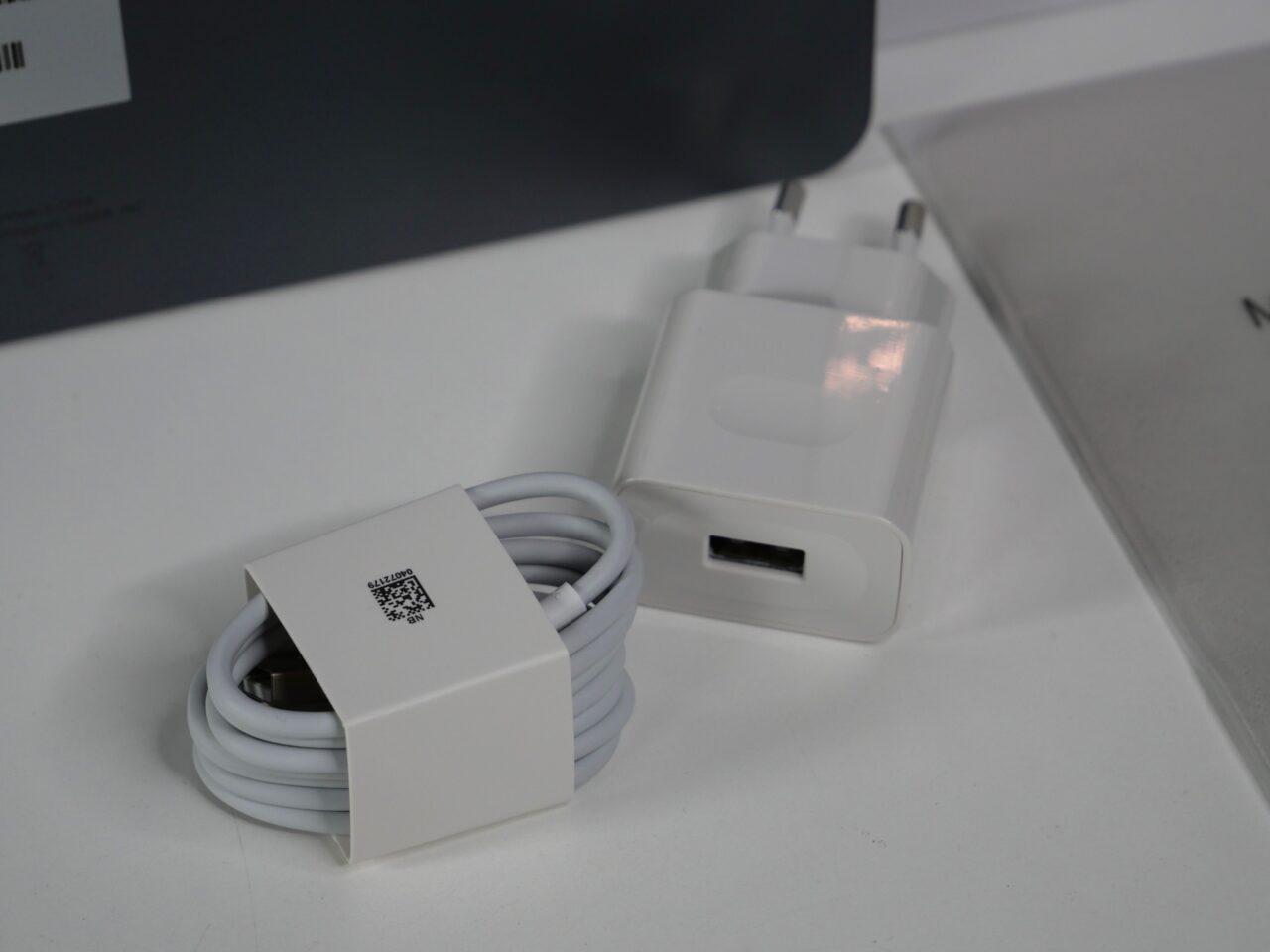Biały adapter do ładowania USB oraz zwinięty kabel z owijką na białym stole.