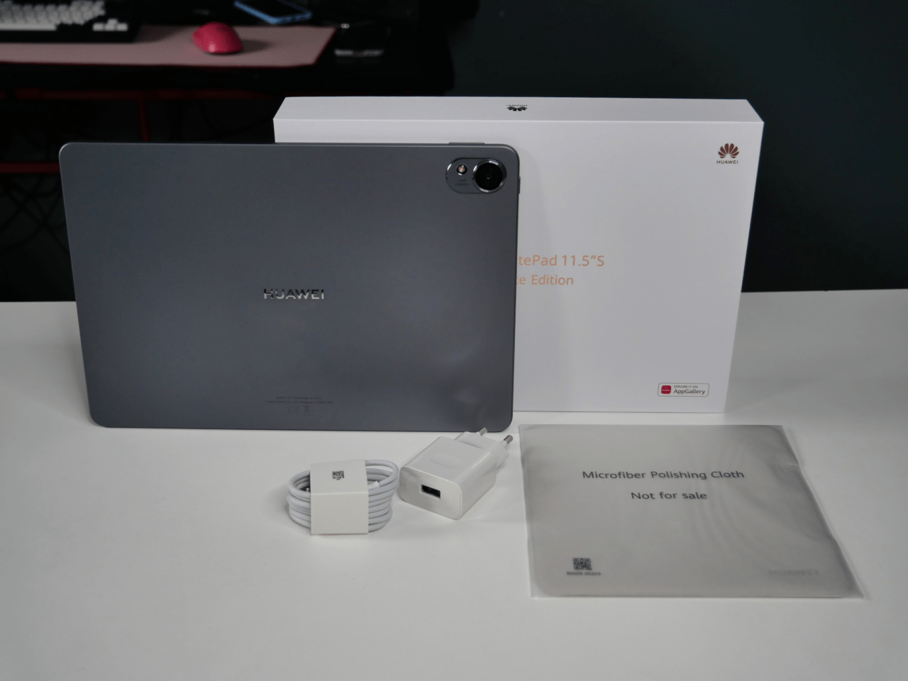 Tablet Huawei z akcesoriami: ładowarką, kablem USB i ściereczką z mikrofibry, oraz pudełkiem w tle.