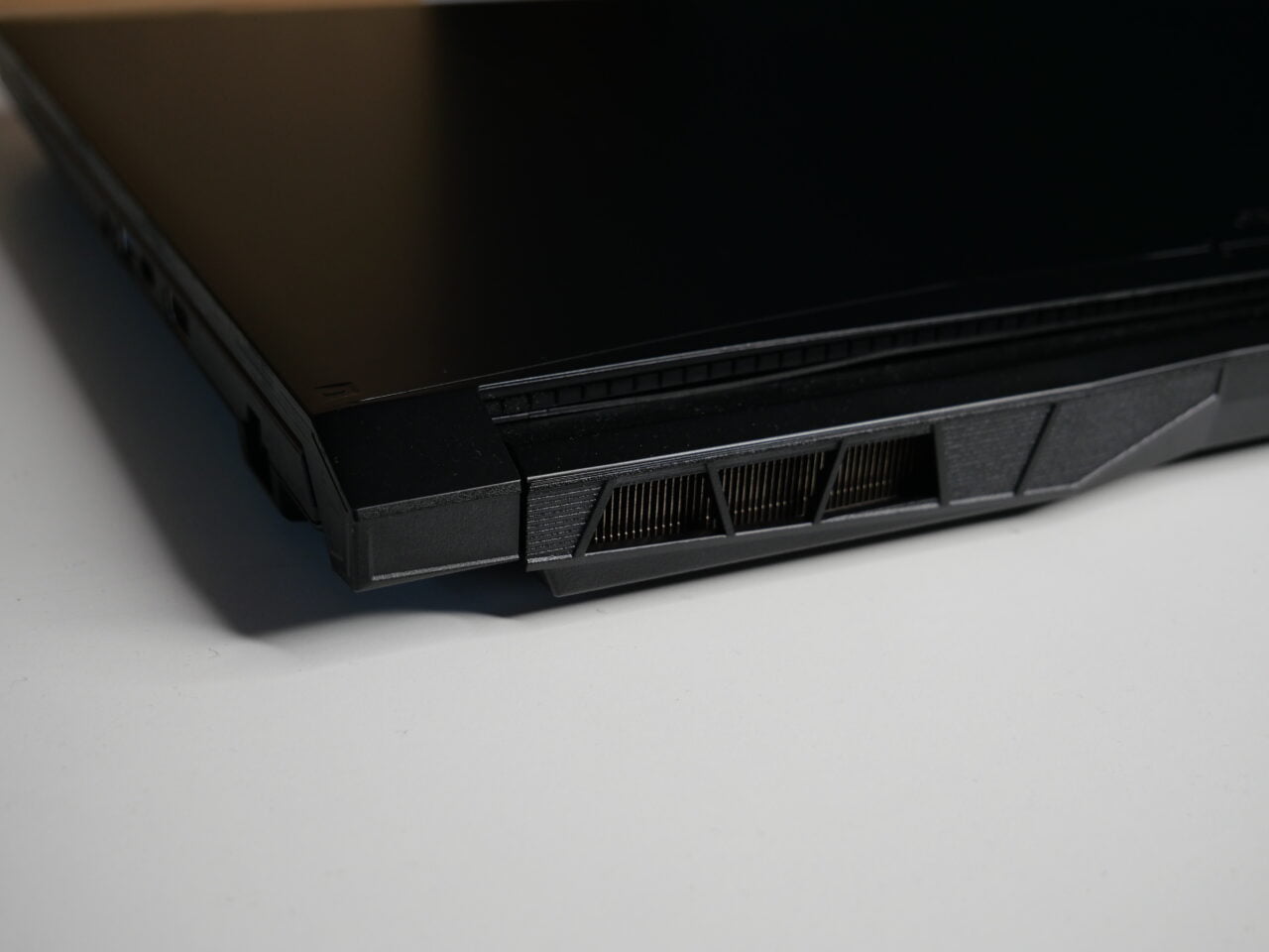 Zbliżenie na tylną część czarnego laptopa, pokazujące otwory wentylacyjne.