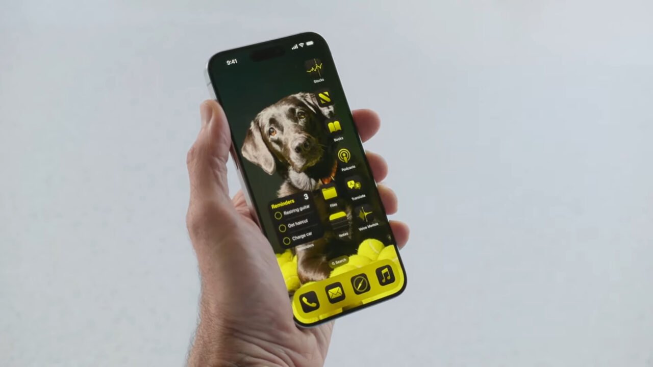 Osoba trzymająca smartfon z widokiem iOS 18 na ekran główny z tapetą przedstawiającą psa.