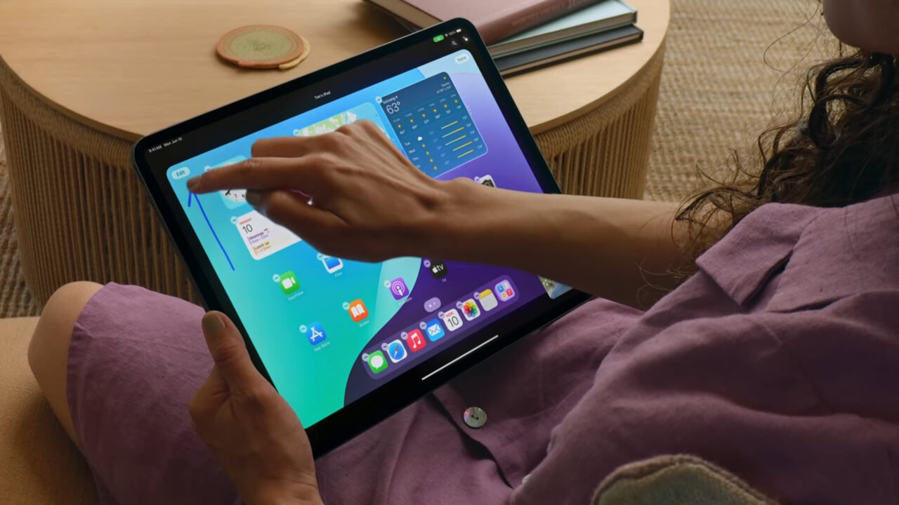 Osoba trzymająca iPada z otwartym pulpitem głównym, na którym widać różne aplikacje i widgety.