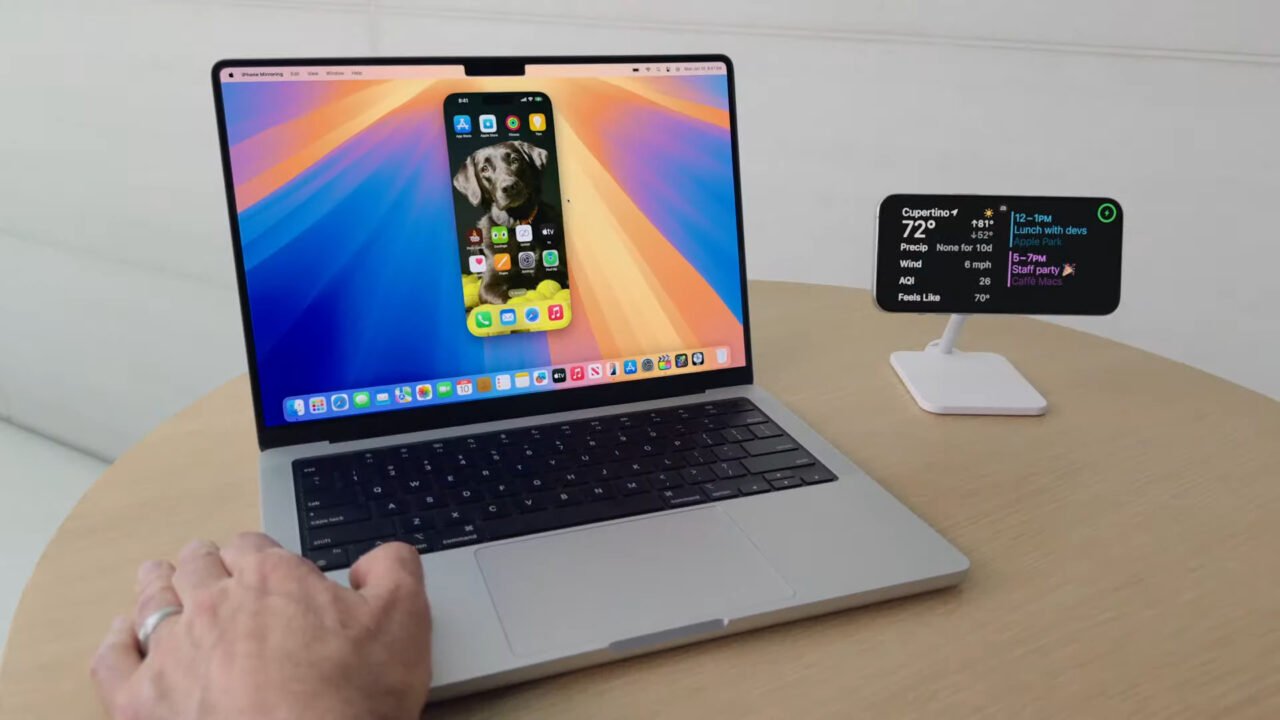 Osoba używająca laptopa na biurku z iPhonem na podstawce obok. Na ekranie laptopa wyświetlany jest pulpit telefonu. Apple odkrywa koło na nowo.