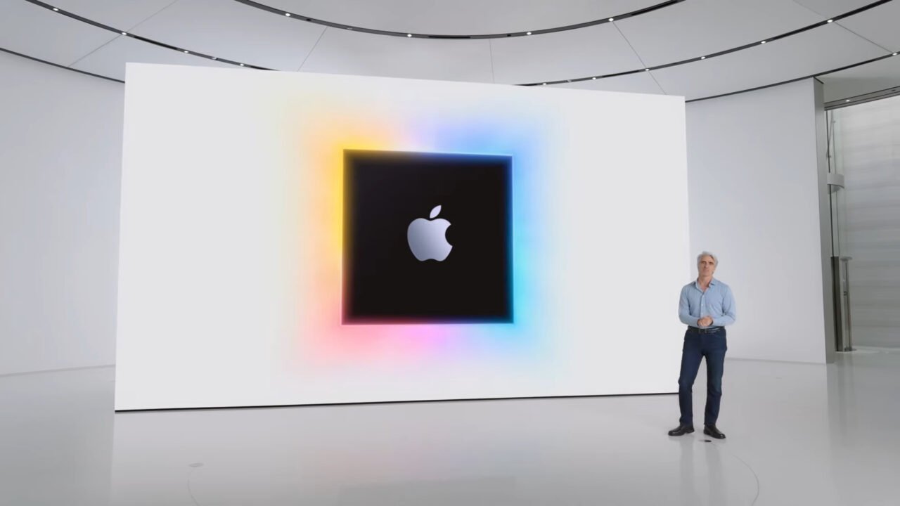 Mężczyzna stojący na scenie przed dużym ekranem z logo Apple.