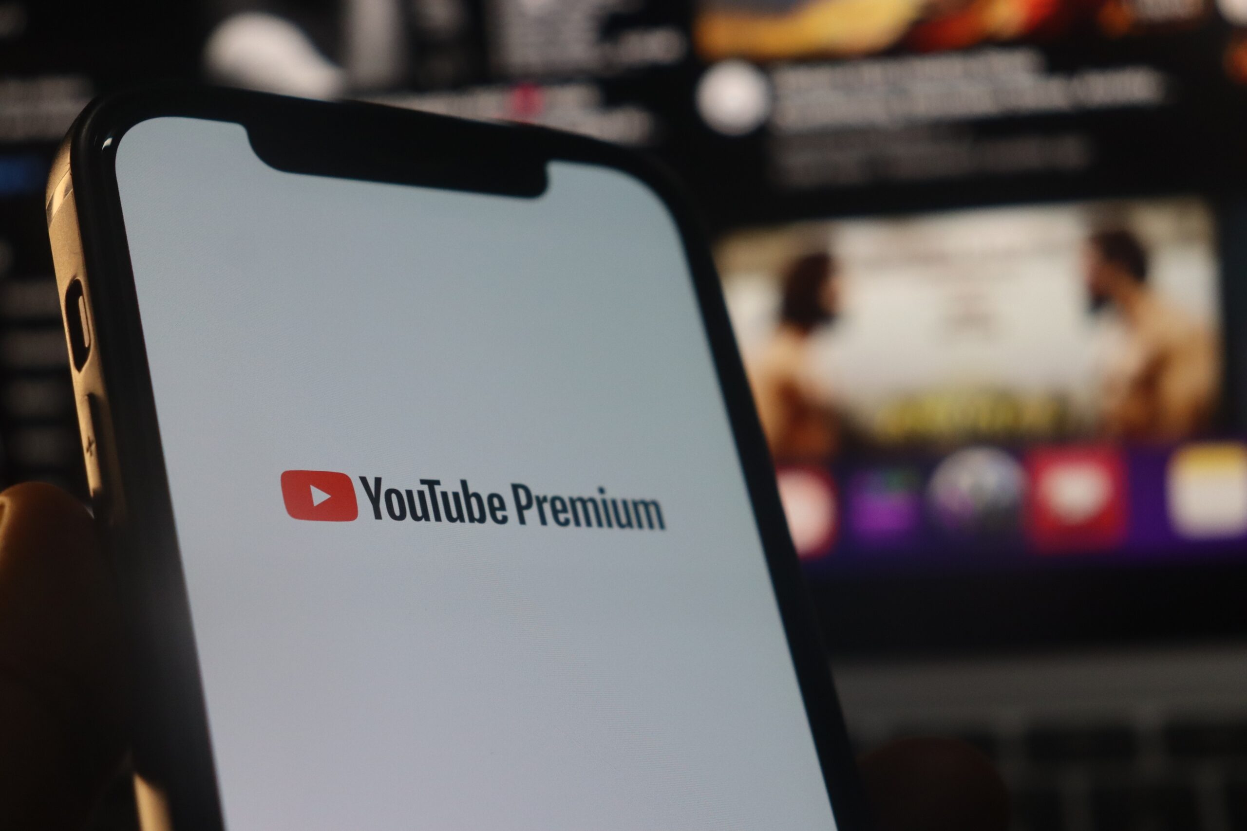 Ekran telefonu z logo YouTube Premium na pierwszym planie, rozmyte tło z odtwarzanym wideo.
