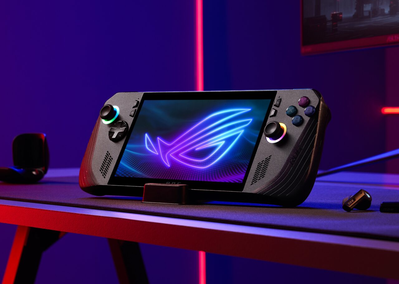 Konsola przenośna do gier na biurku, z kolorowym logo na ekranie, w tle ciemne niebieskie i czerwone światła.