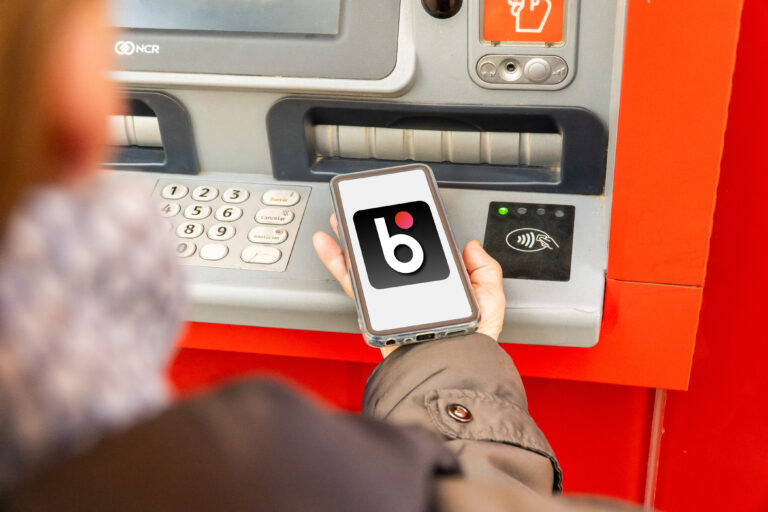 Osoba trzymająca telefon przed bankomatem z funkcją płatności zbliżeniowych.