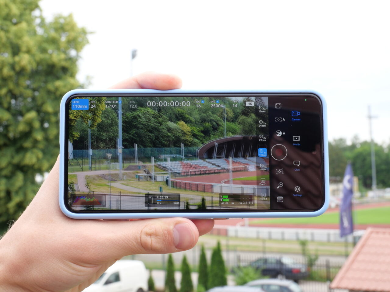 Telefon w ręku z uruchomioną aplikacją aparatu, pokazujący nagrywanie stadionu sportowego w tle.