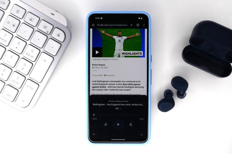 Smartfon na białym tle z otwartą stroną BBC sport, obok klawiatury i słuchawek bezprzewodowych.