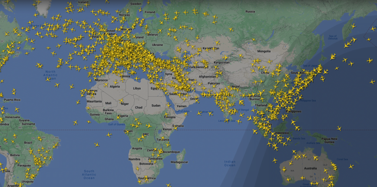 Mapa świata z mnogością żółtych ikonek samolotów wskazujących na aktualne loty samolotów komercyjnych.