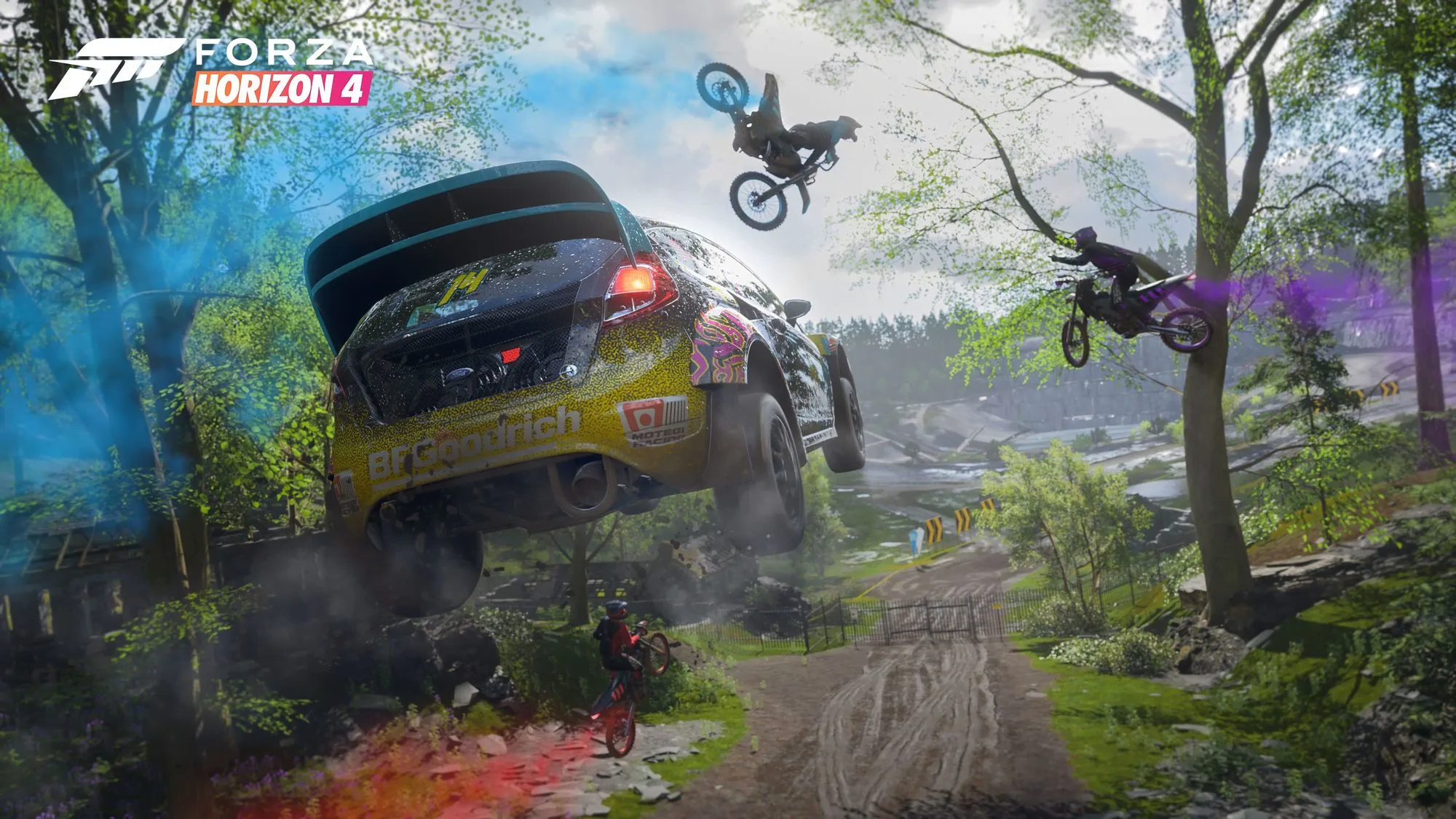 Samochód rajdowy w locie oraz motocykliści wykonujący akrobacje w grze Forza Horizon 4 w lesie.