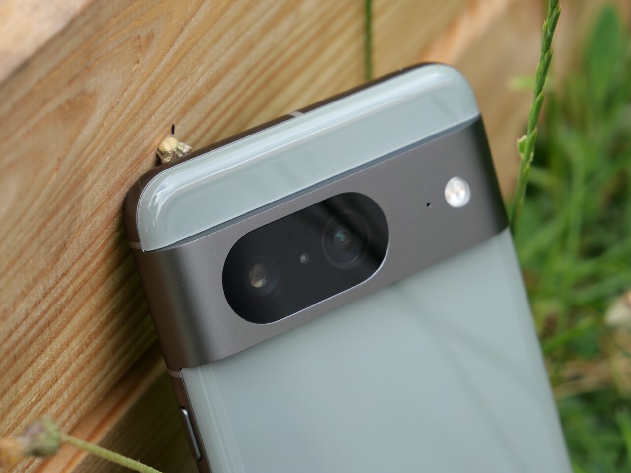 Telefon komórkowy z aparatem leżący na drewnianej powierzchni obok trawy.