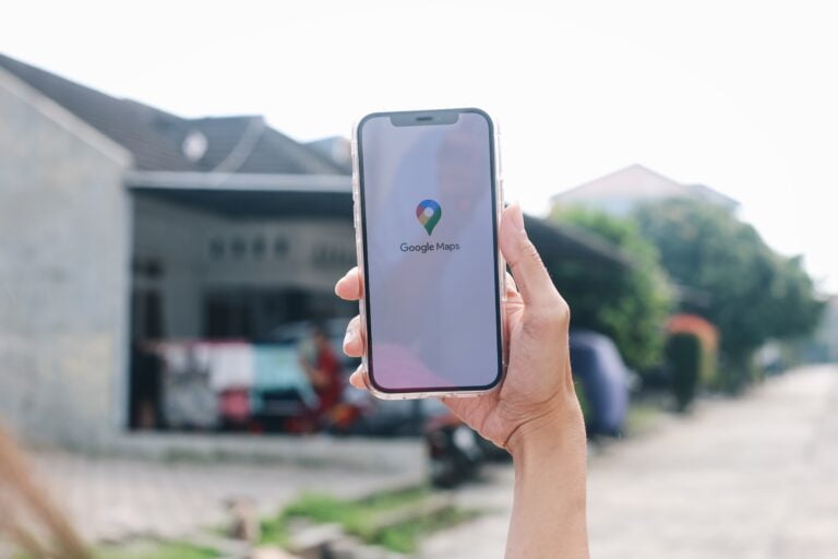 Osoba trzymająca smartfona z logo Google Maps na ekranie, w tle domy.