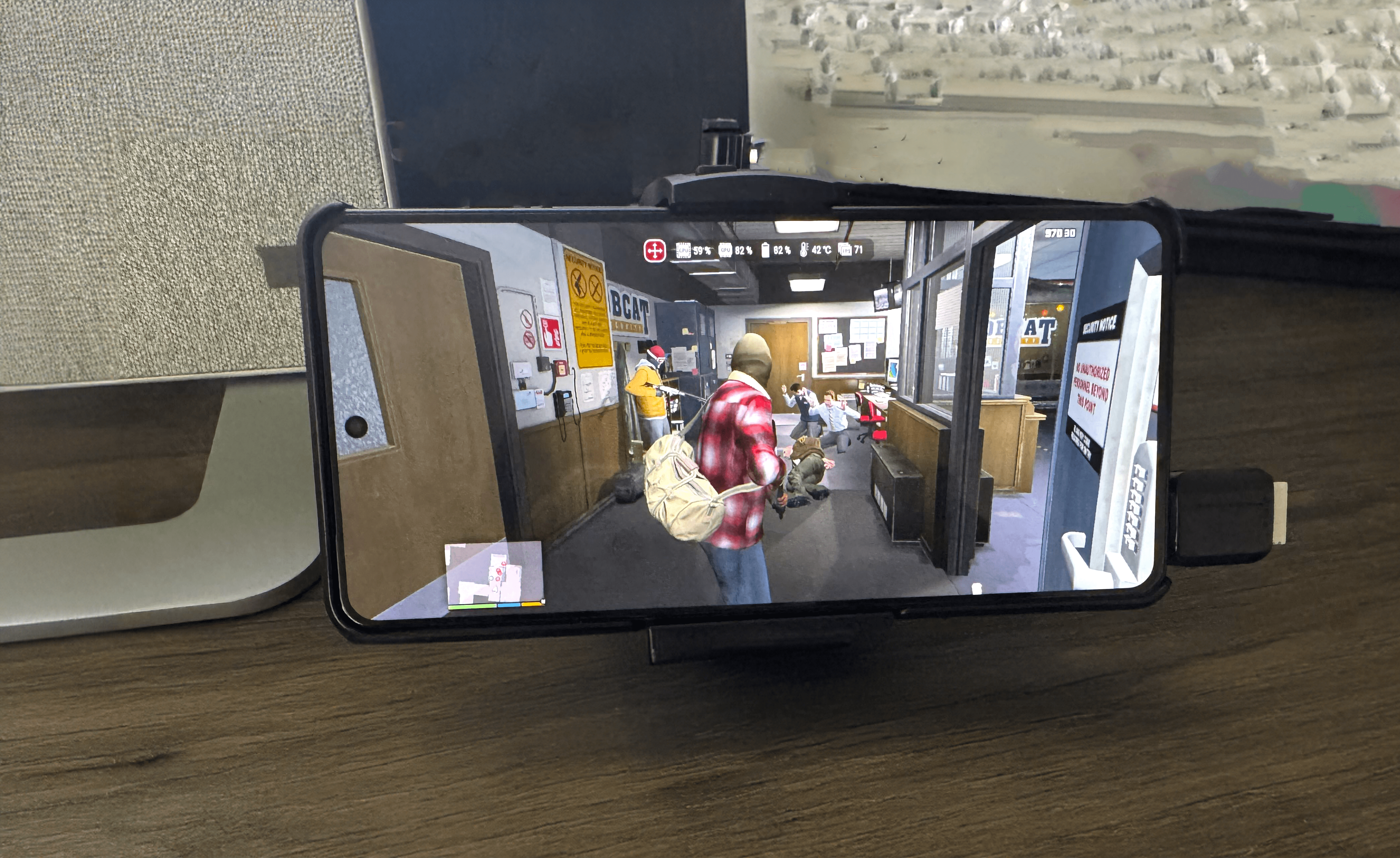 Smartfon wyświetlający grę wideo, na biurku z monitorem i klawiaturą w tle.