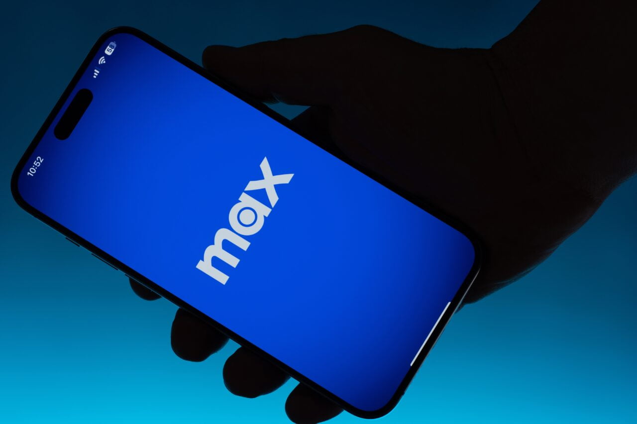 Ręka trzymająca smartfon z włączonym ekranem z logo "max" na niebieskim tle. Aplikacja zastąpi HBO Max