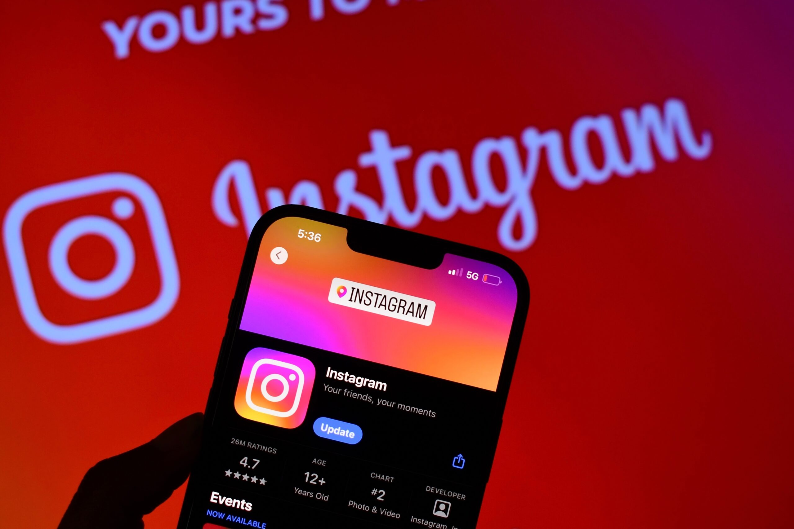 Aplikacja Instagram na ekranie smartfona na tle rozmytego logotypu Instagram z czerwonym tłem.
