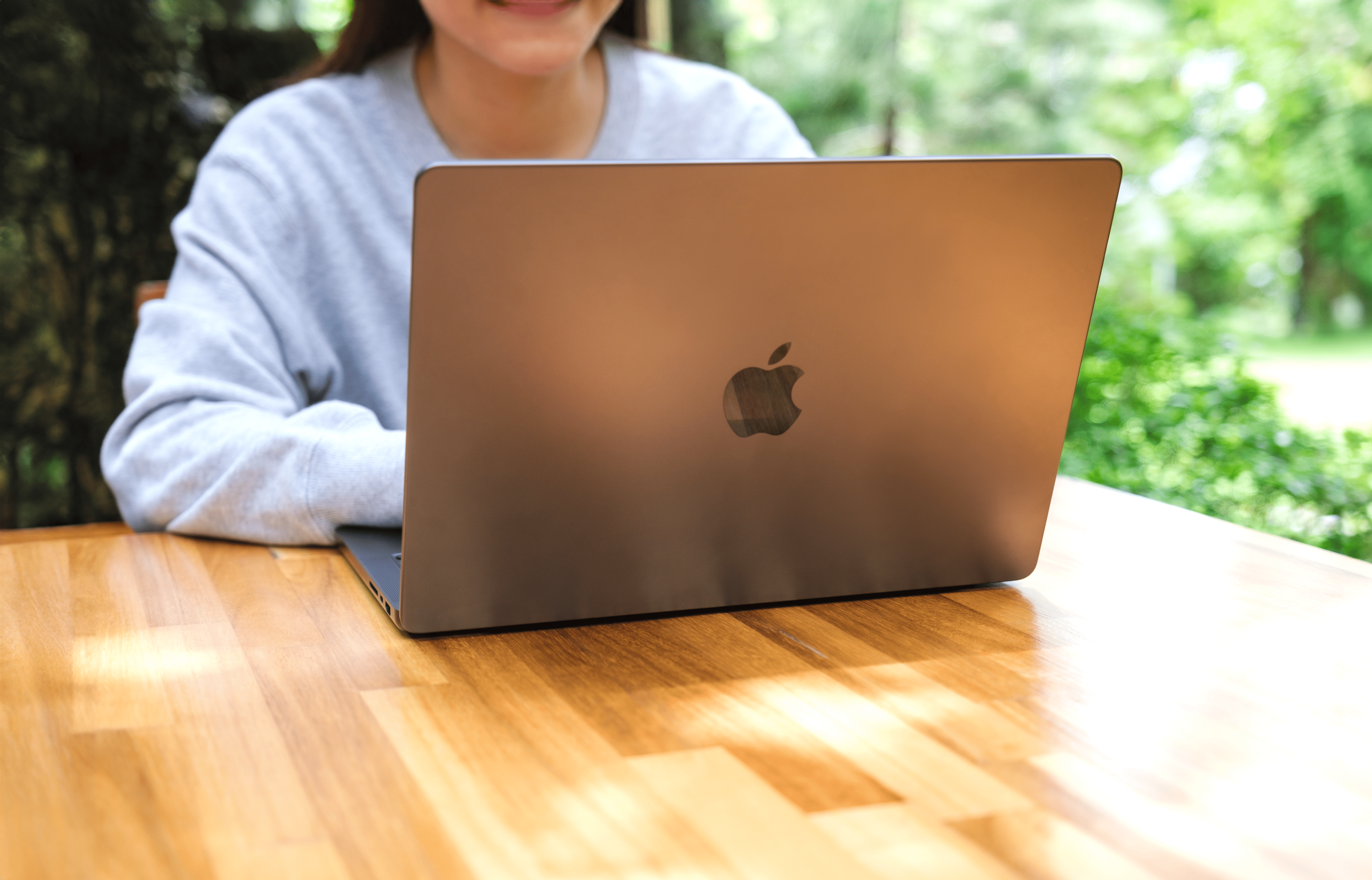 Kobieta używająca komputra Apple MacBook Air M1 na drewnianym stole.