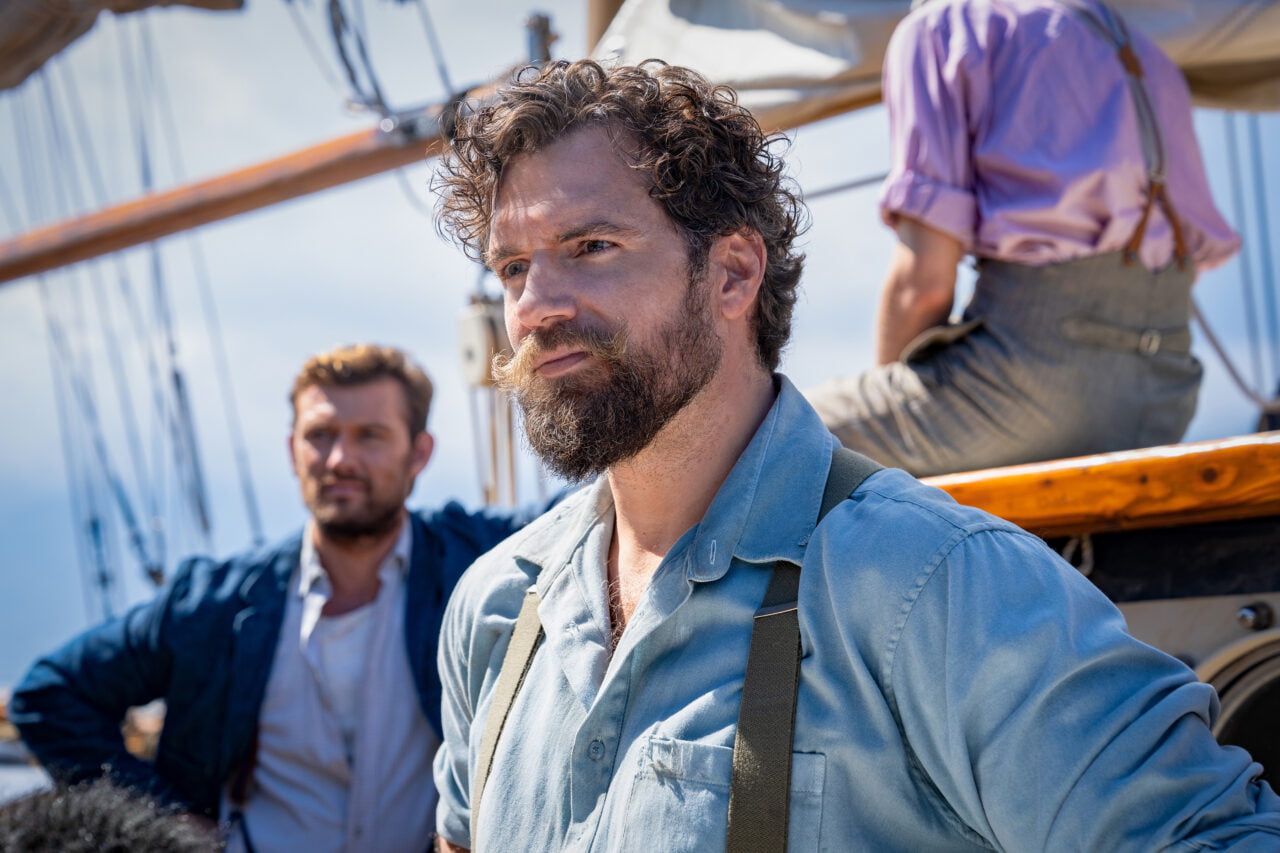 Ministerstwo Niebezpiecznych Drani - Henry Cavill z brodą i wąsami na statku patrzy w dal, w tle inny mężczyzna oparty o reling.